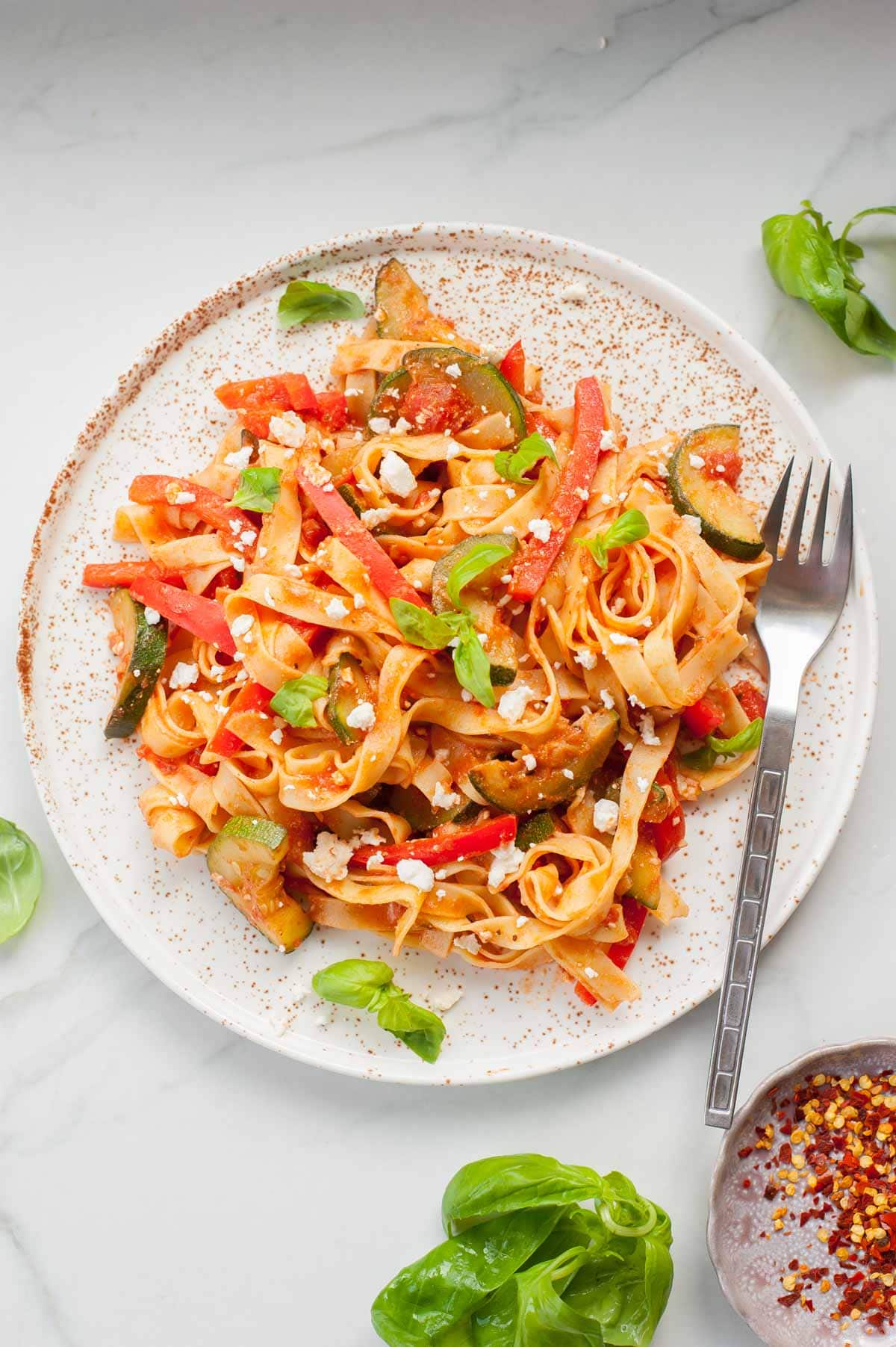 Tagliatelle pasta with zucchini, bell pepper and feta on a white plate.