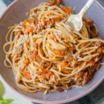 Spaghetti with fresh tomato meat sauce on a fork in a violet bowl.