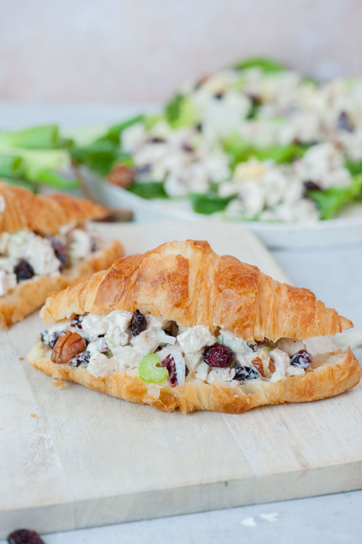 Croissant sandwich with cranberry chicken salad on a beige wooden board.