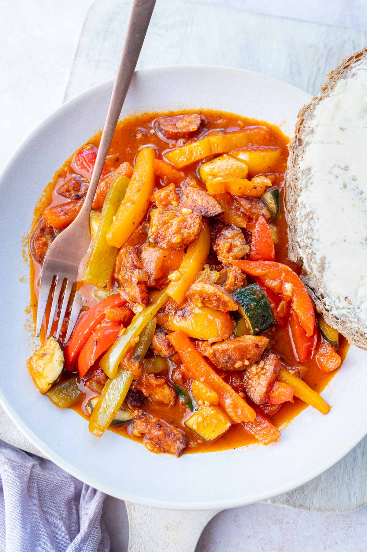 Leczo (Polish stew) in a white bowl with a piece of bread on the side.