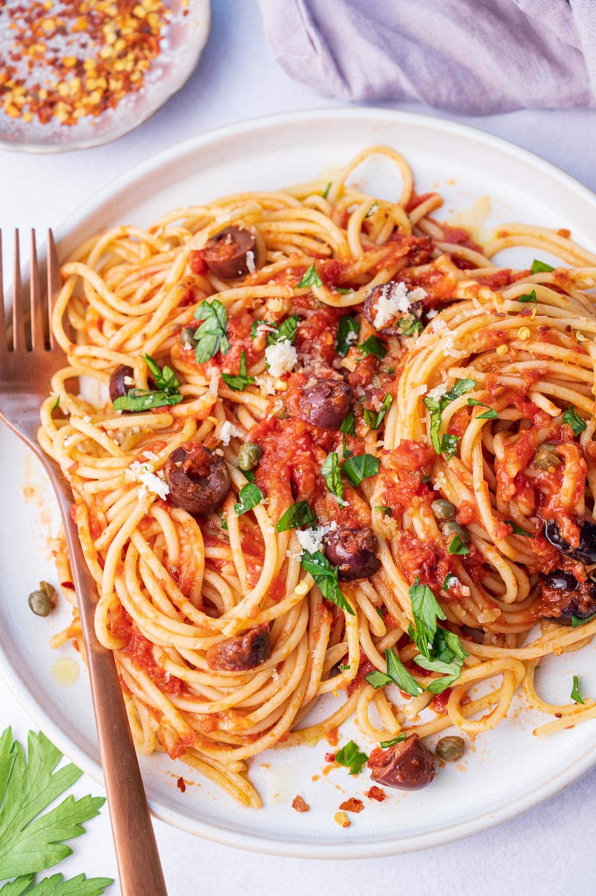 Pasta puttanesca on a white plate.