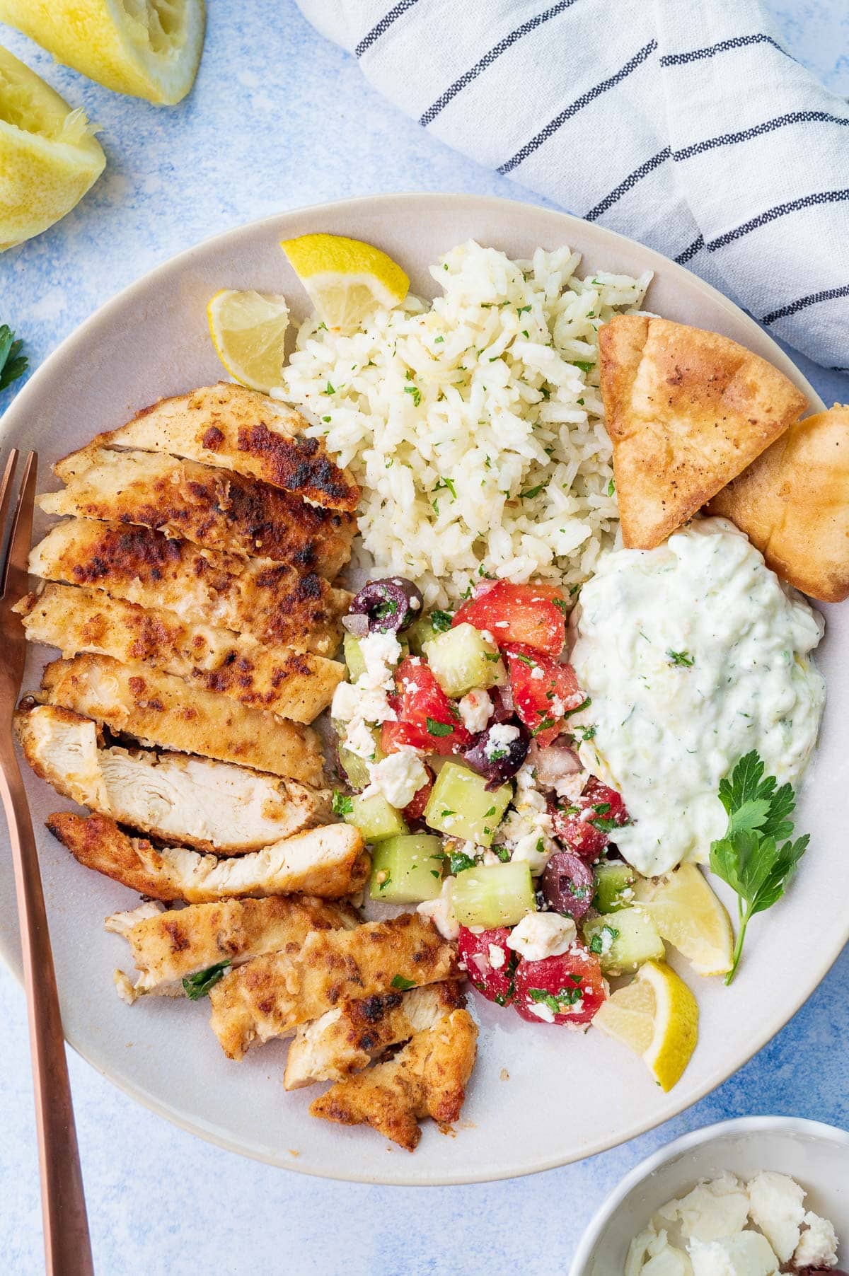 A bowl with Greek chicken, Greek salad, lemon rice, and tzatziki.