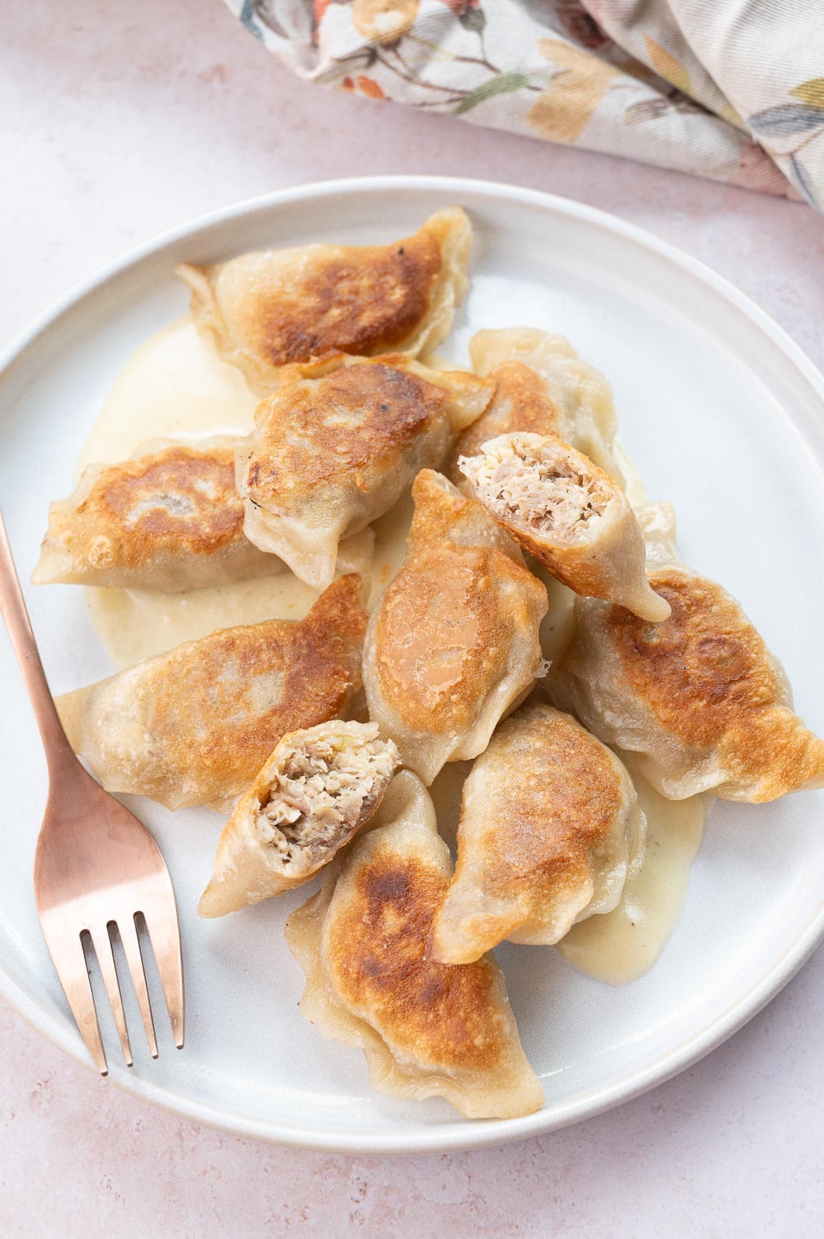 Meat pierogi with cheese sauce on a white plate.