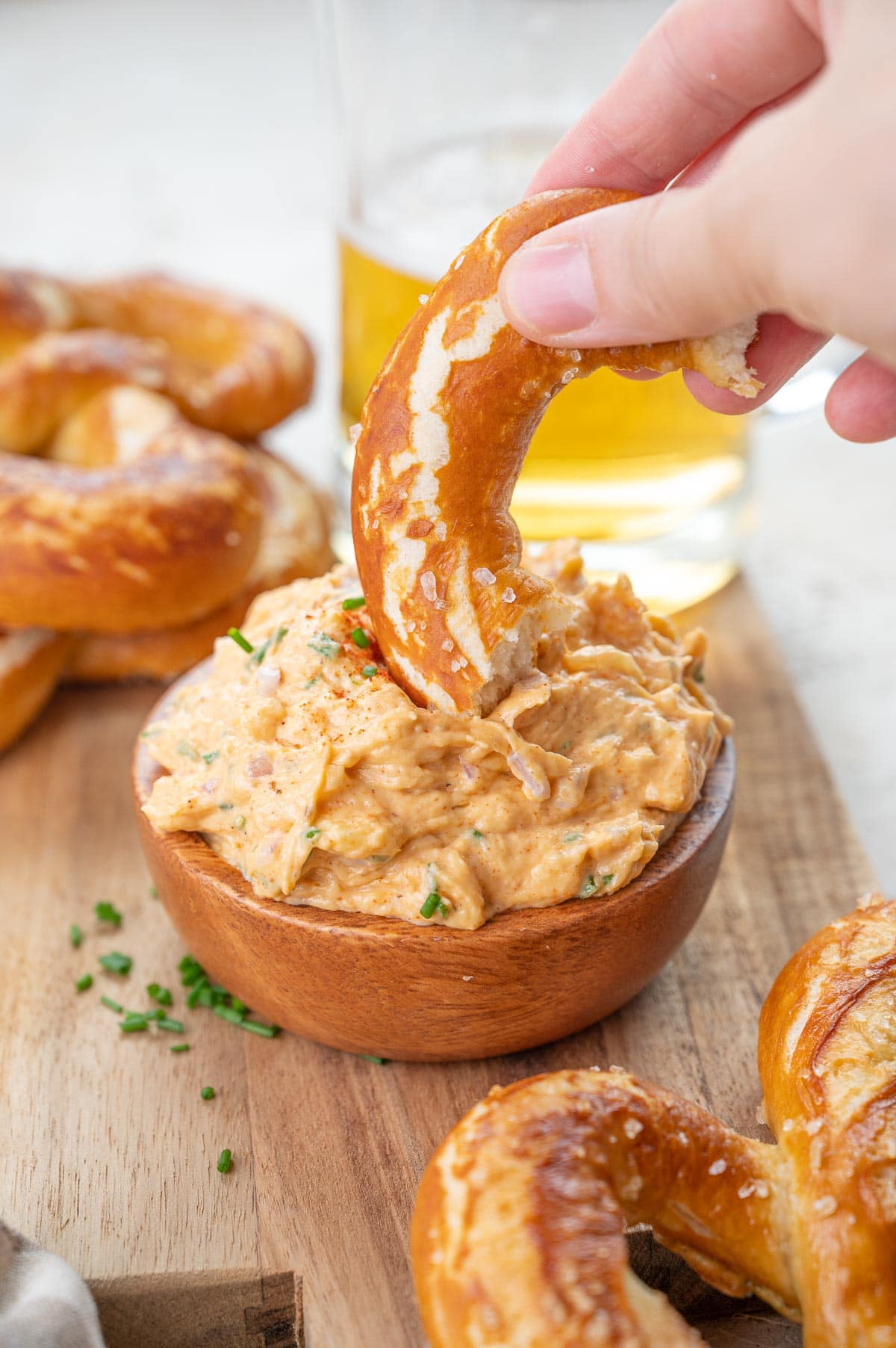 A piece of a soft pretzel is being dipped in Obatzda dip.