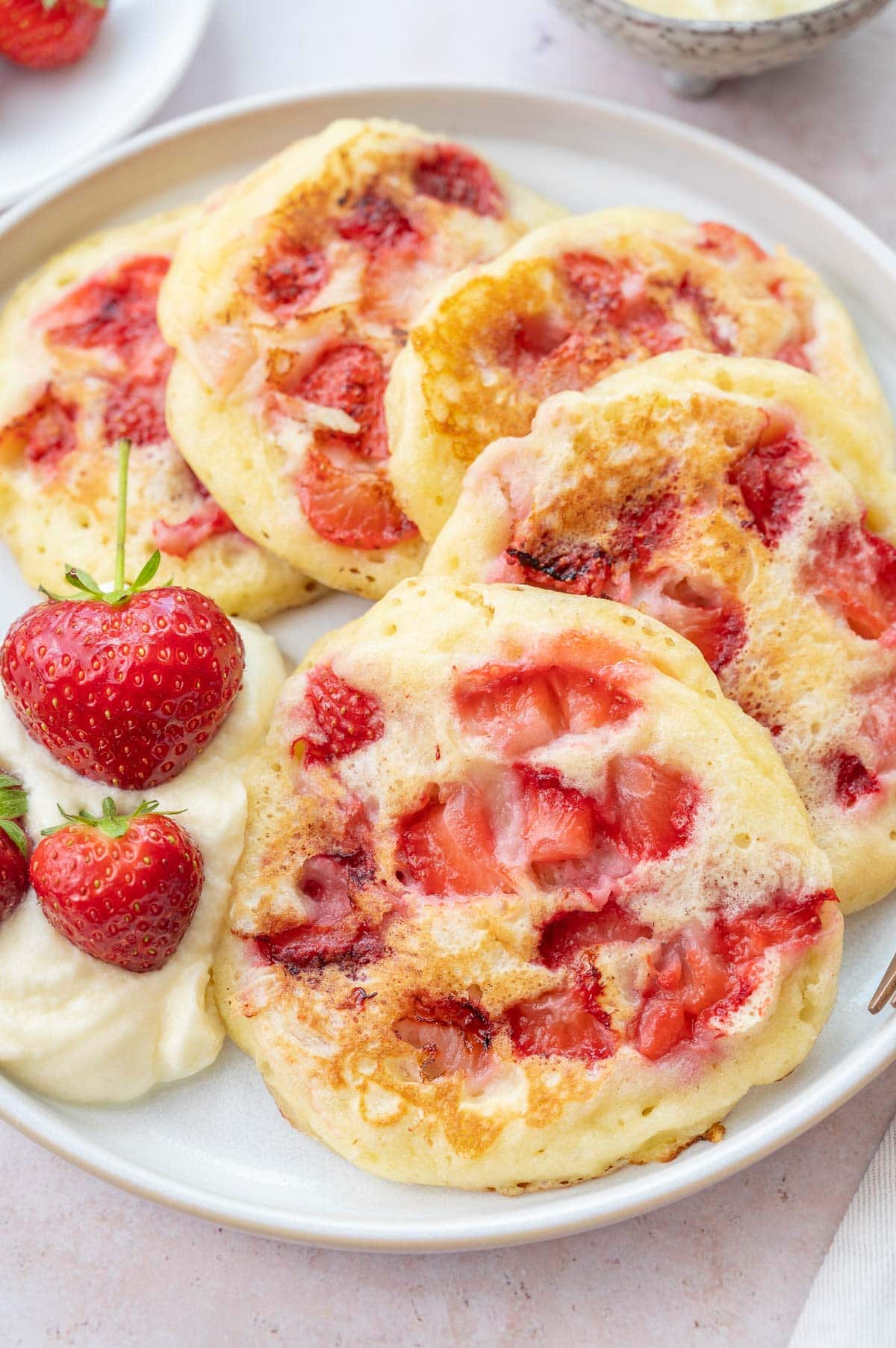 Strawberry pancakes on a white plate with a dollop of whipped cream on the side.