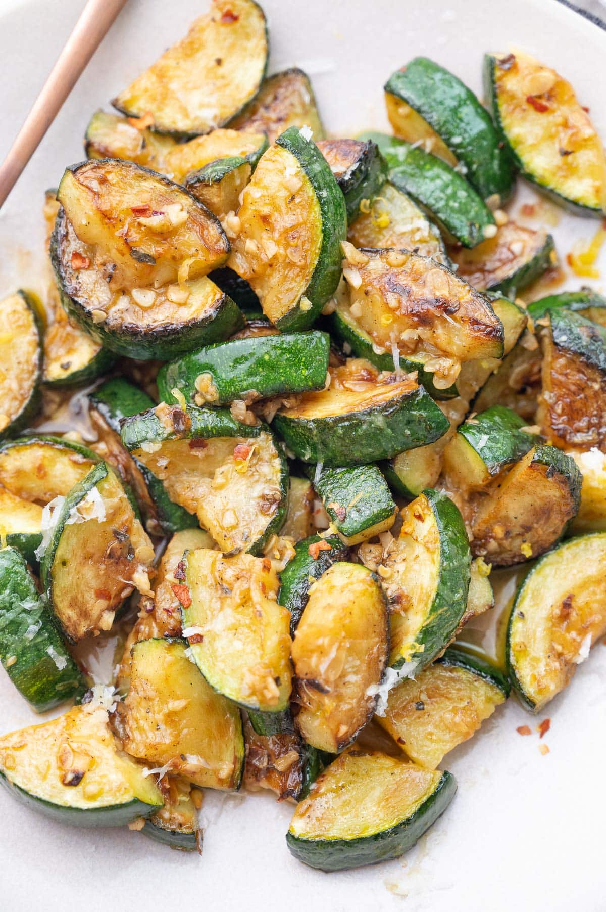 Sauteed zucchini with lemon, garlic, red pepper flakes, and cheese on a white plate.