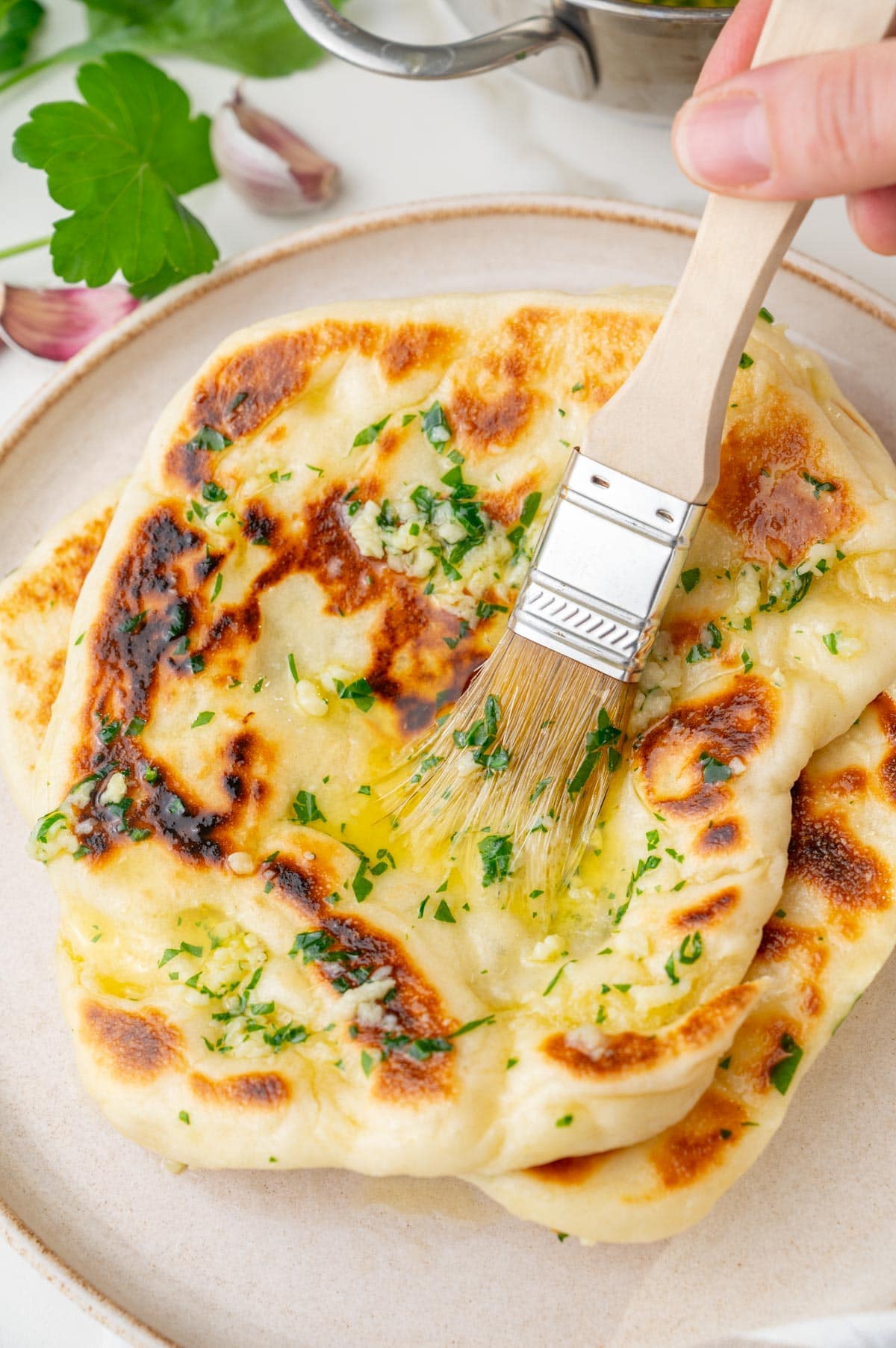 Naan bread is being brushed with garlic butter.