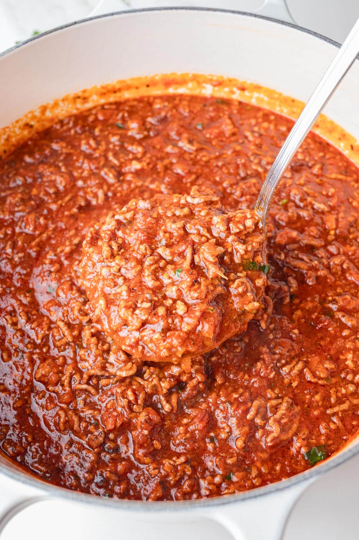 Spaghetti meat sauce in a white pot with a ladle inside.